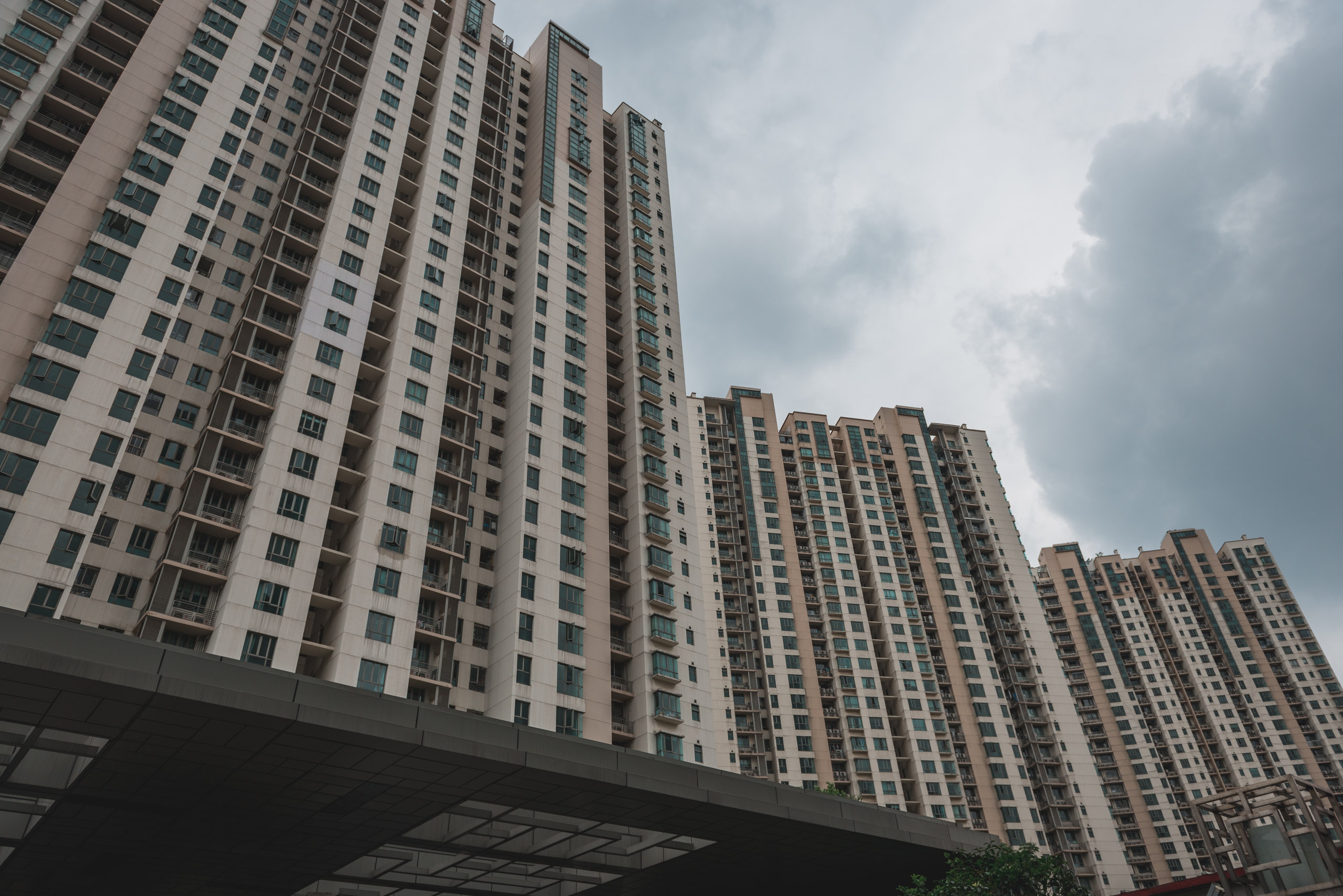 Multiple residential high-rise apartment towers with uniform white and tan facades rise against an overcast sky, their repetitive grid of windows creating geometric patterns across the urban landscape