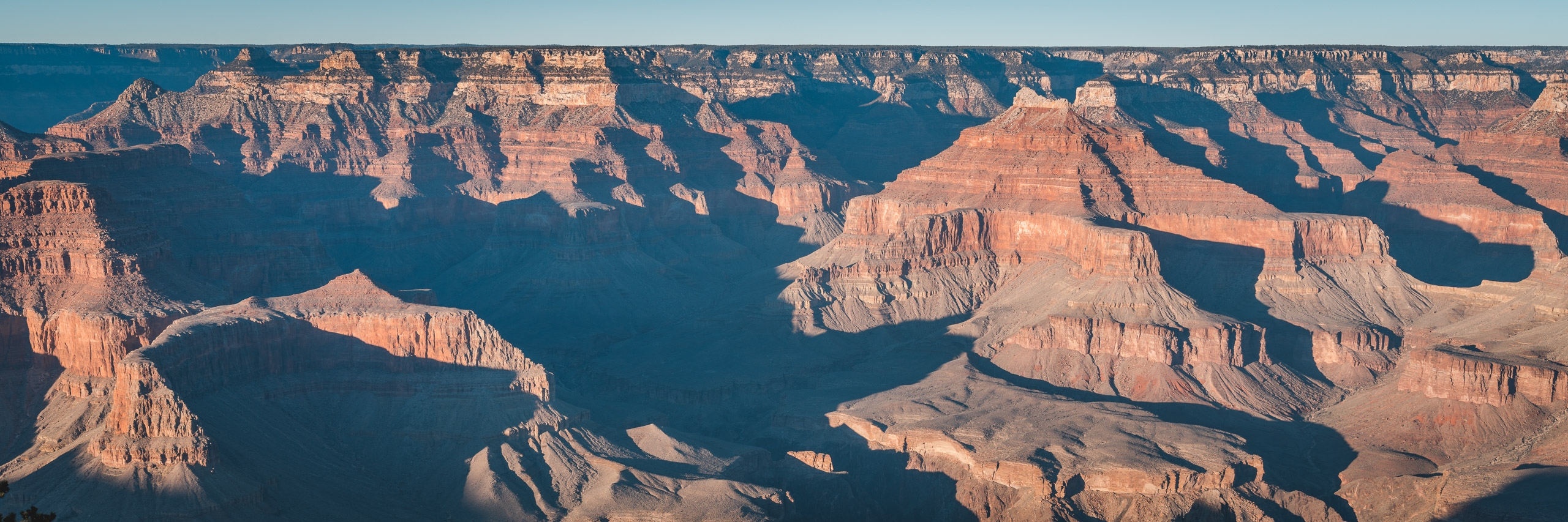 Layered rock formations and deep shadows create dramatic contrast across the Grand Canyon's vast expanse, with warm golden cliffs illuminated against deep blue shadowed valleys