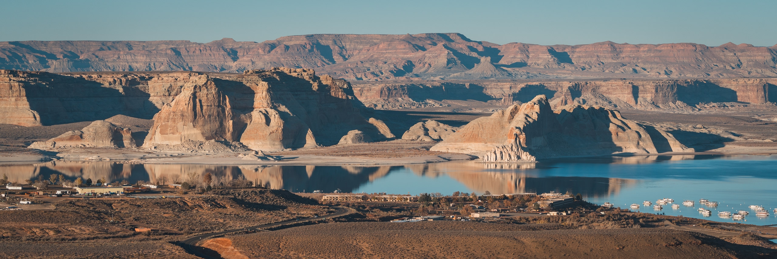 A sprawling desert landscape reveals Band-i-Amir Lake's turquoise waters nestled beneath towering sandstone buttes and mesas under clear blue sky