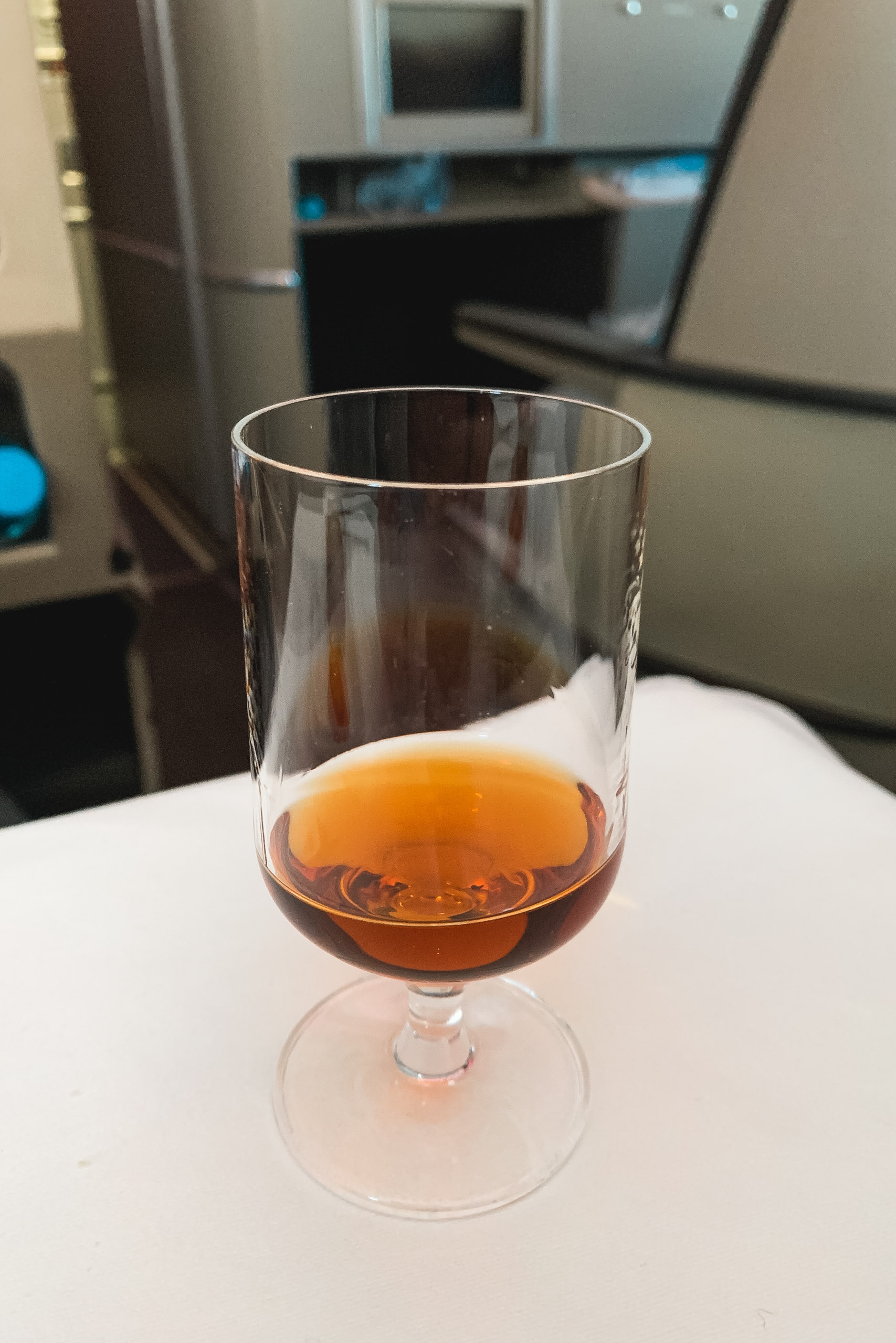 A stemmed glass filled with amber liquid sits on a white surface with kitchen appliances blurred in the background