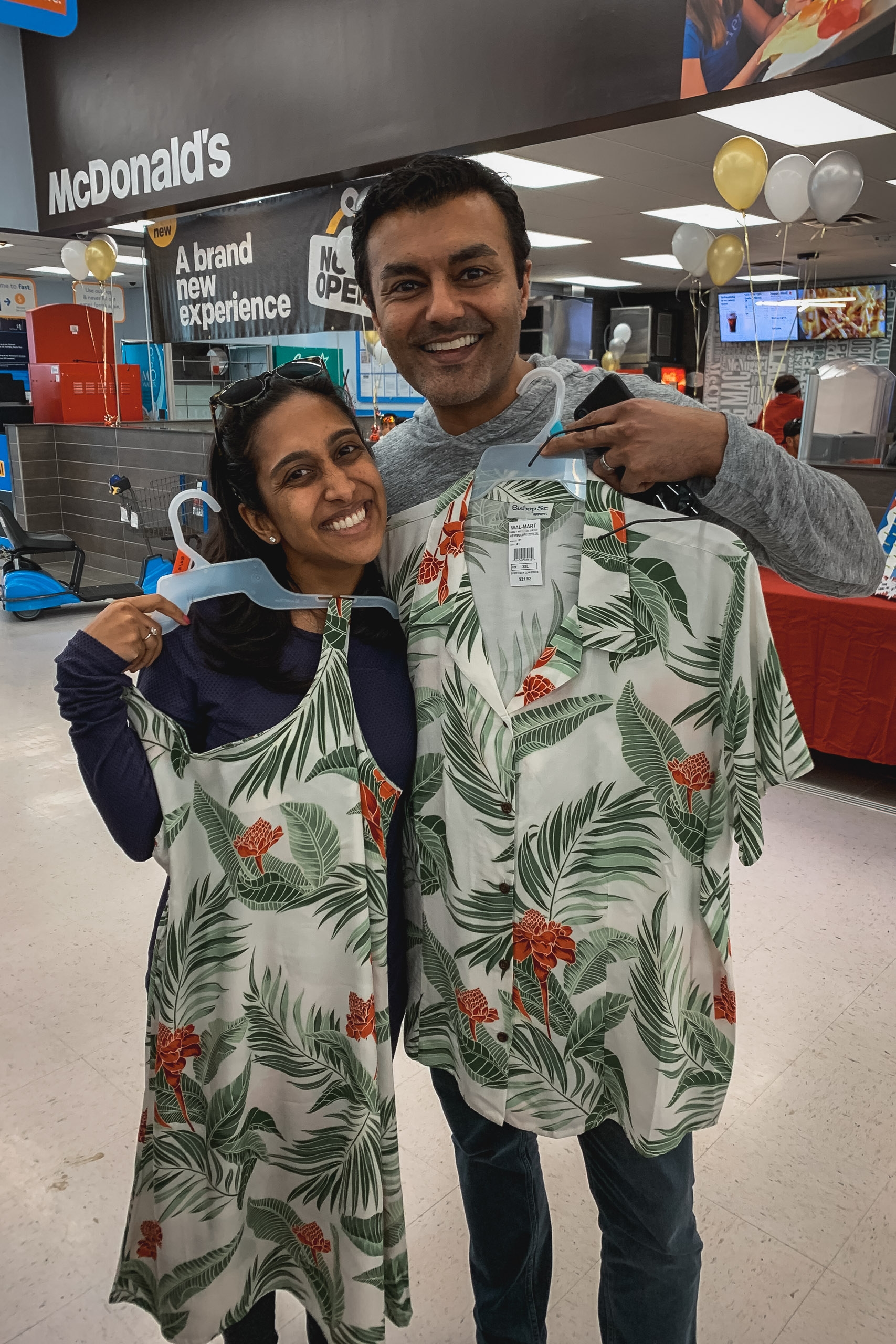 Two smiling people hold up a tropical leaf-patterned blanket or garment inside a McDonald's restaurant with bright overhead lighting and branded signage visible in the background