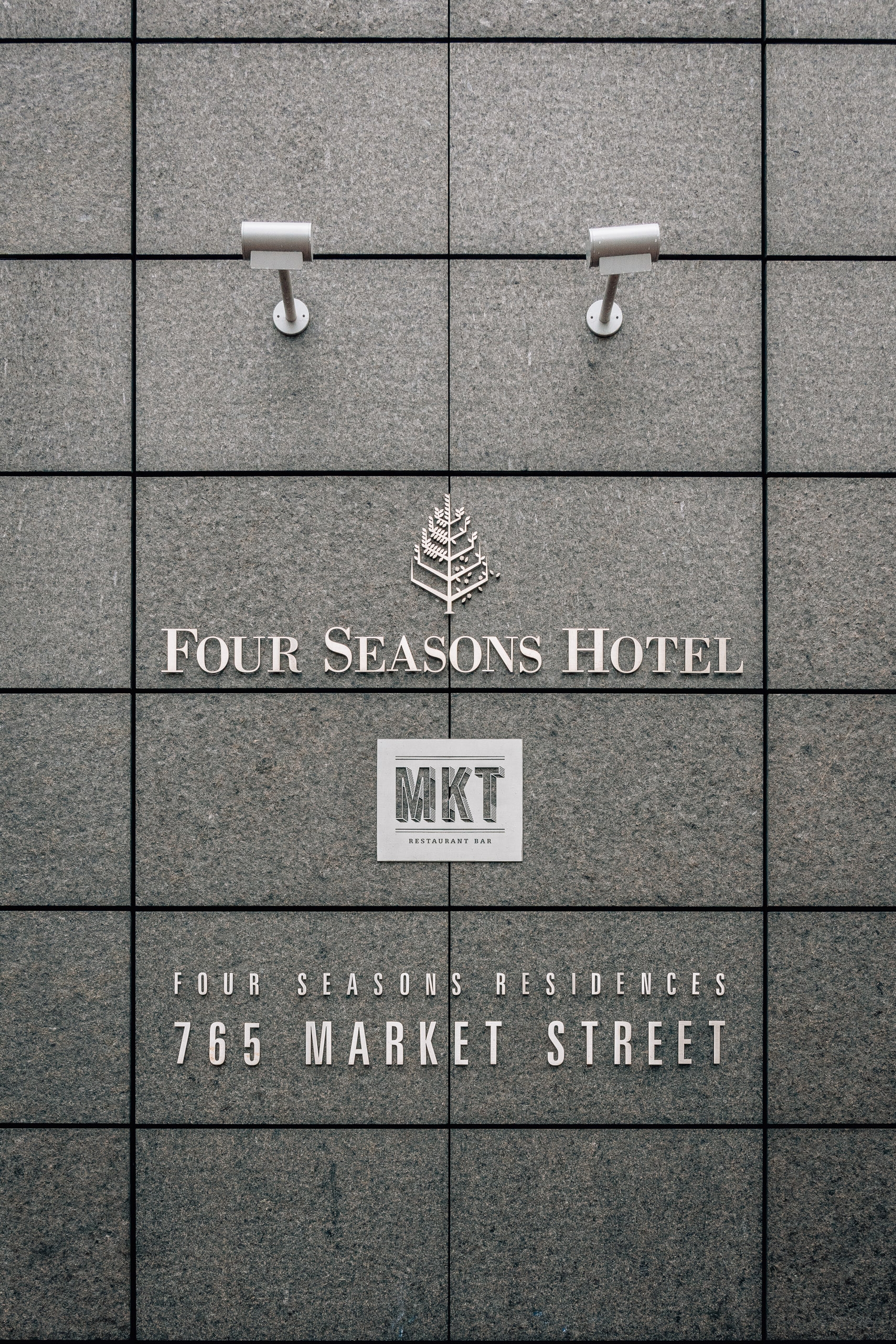 Minimalist facade of Four Seasons Hotel and Residences displays signage on gray tile wall with two white handles above the entrance marking at 765 Market Street