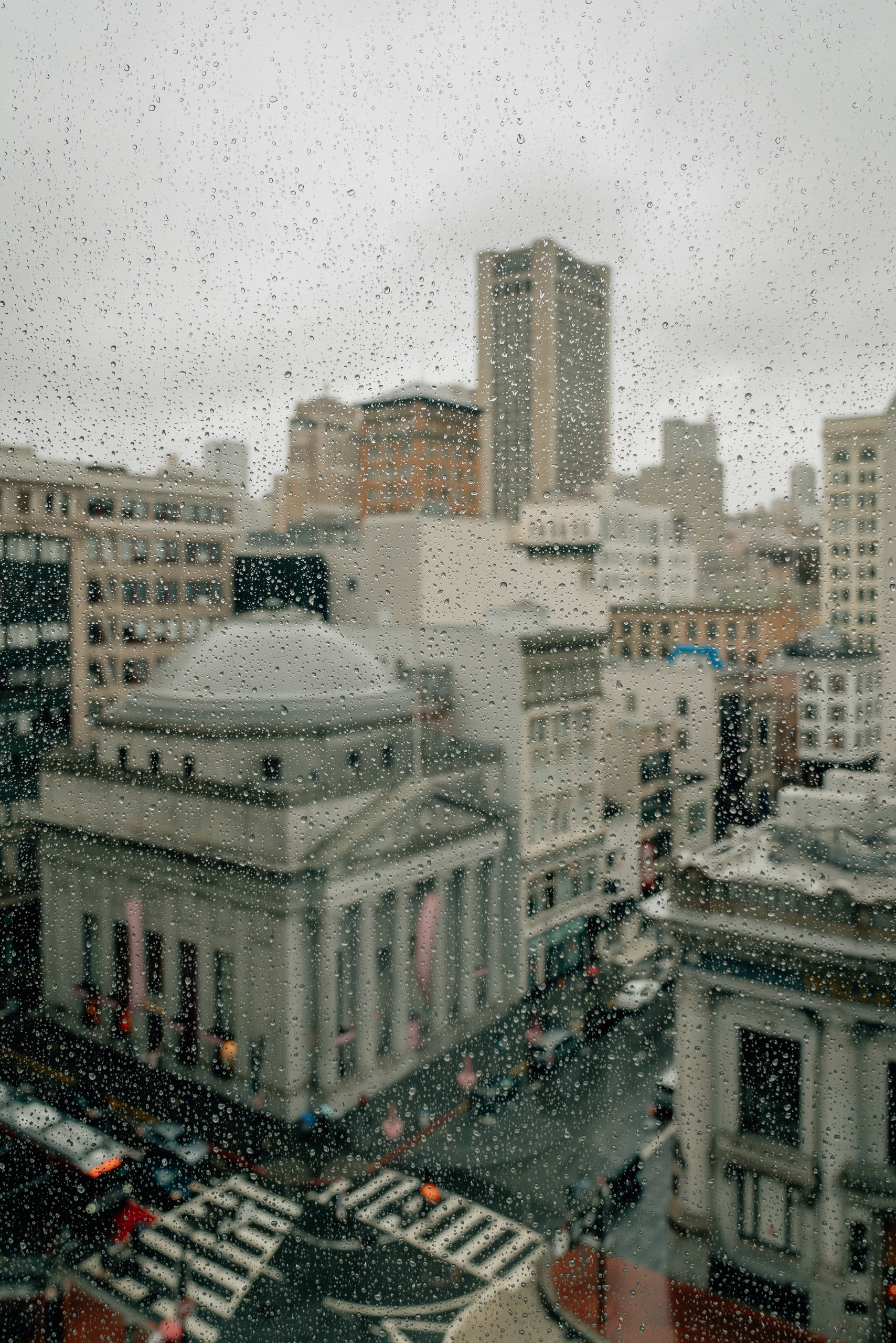 Urban cityscape with classical building and modern skyscrapers visible through a rain-covered window, showing wet streets and crosswalks below