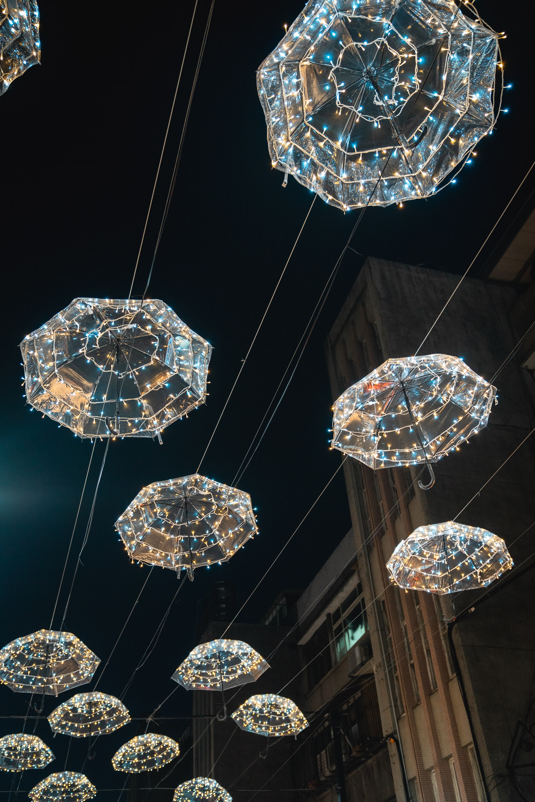 Illuminated decorative umbrellas suspended above a Taipei street at night, their warm and cool-toned lights creating a festive canopy against dark buildings and sky