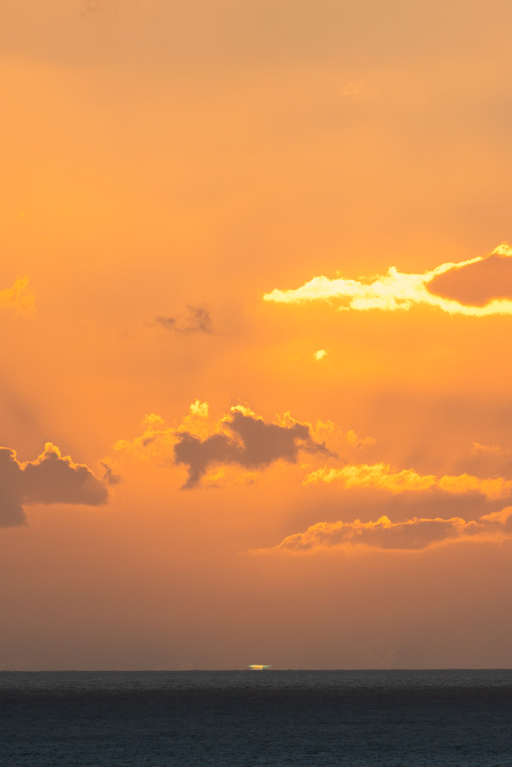 Golden sunset light breaks through dramatic clouds above a dark ocean horizon, casting warm amber tones across the sky and water below