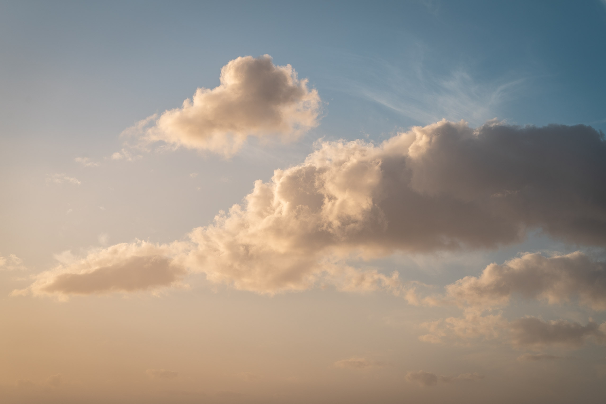 Towering cumulus clouds catch warm golden sunlight against a pale blue sky, with soft shadows defining their billowing peaks and valleys