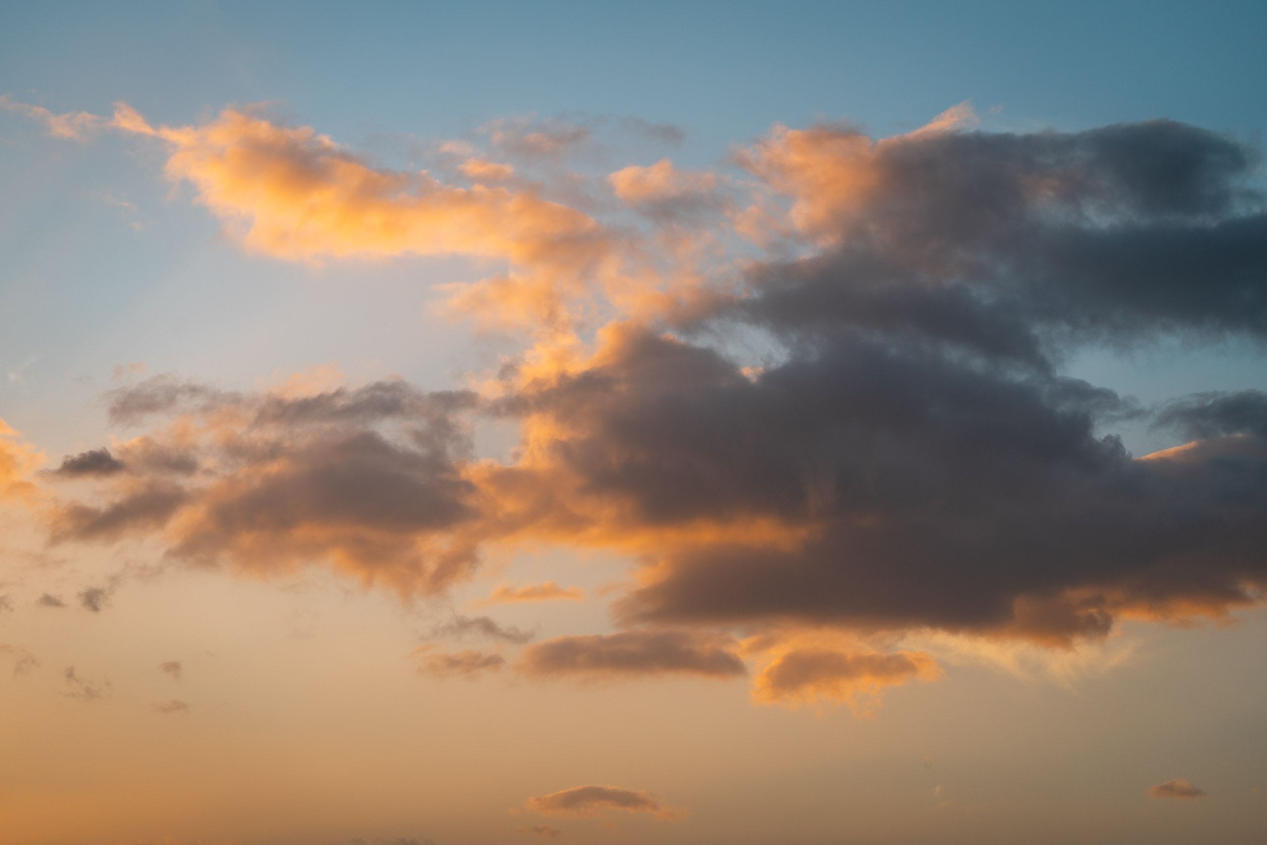 Golden sunset light illuminates towering clouds against a gradient sky, transitioning from warm orange near the horizon to cool blue at the top