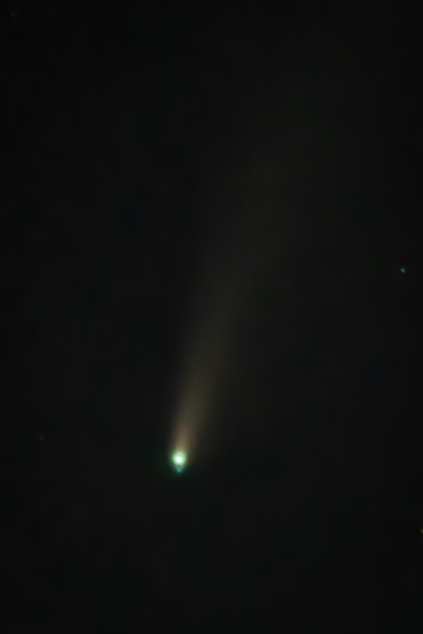 A comet with a greenish coma and tan-brown tail streaks diagonally upward through a dark night sky, with a faint star visible in the upper right corner