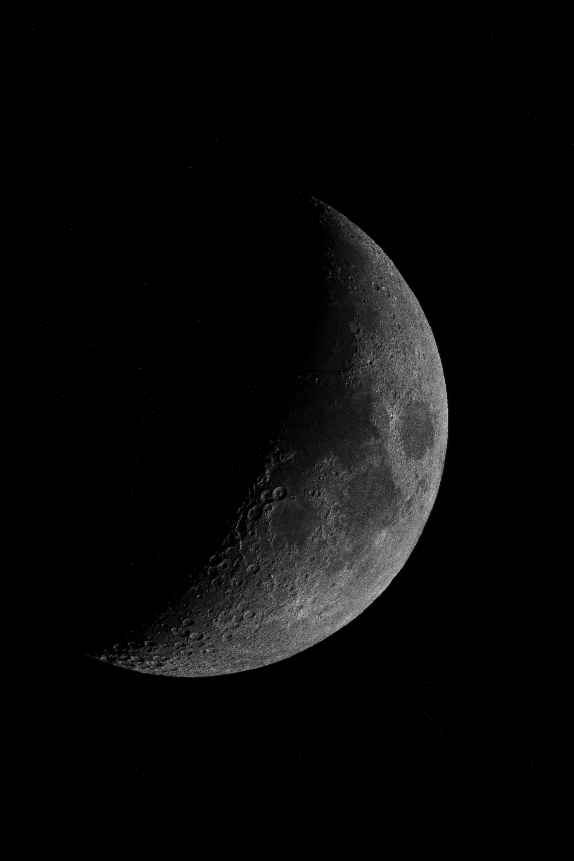 A waxing crescent moon with detailed surface texture and cratering emerges against a black night sky, illuminated by sunlight along its curved edge