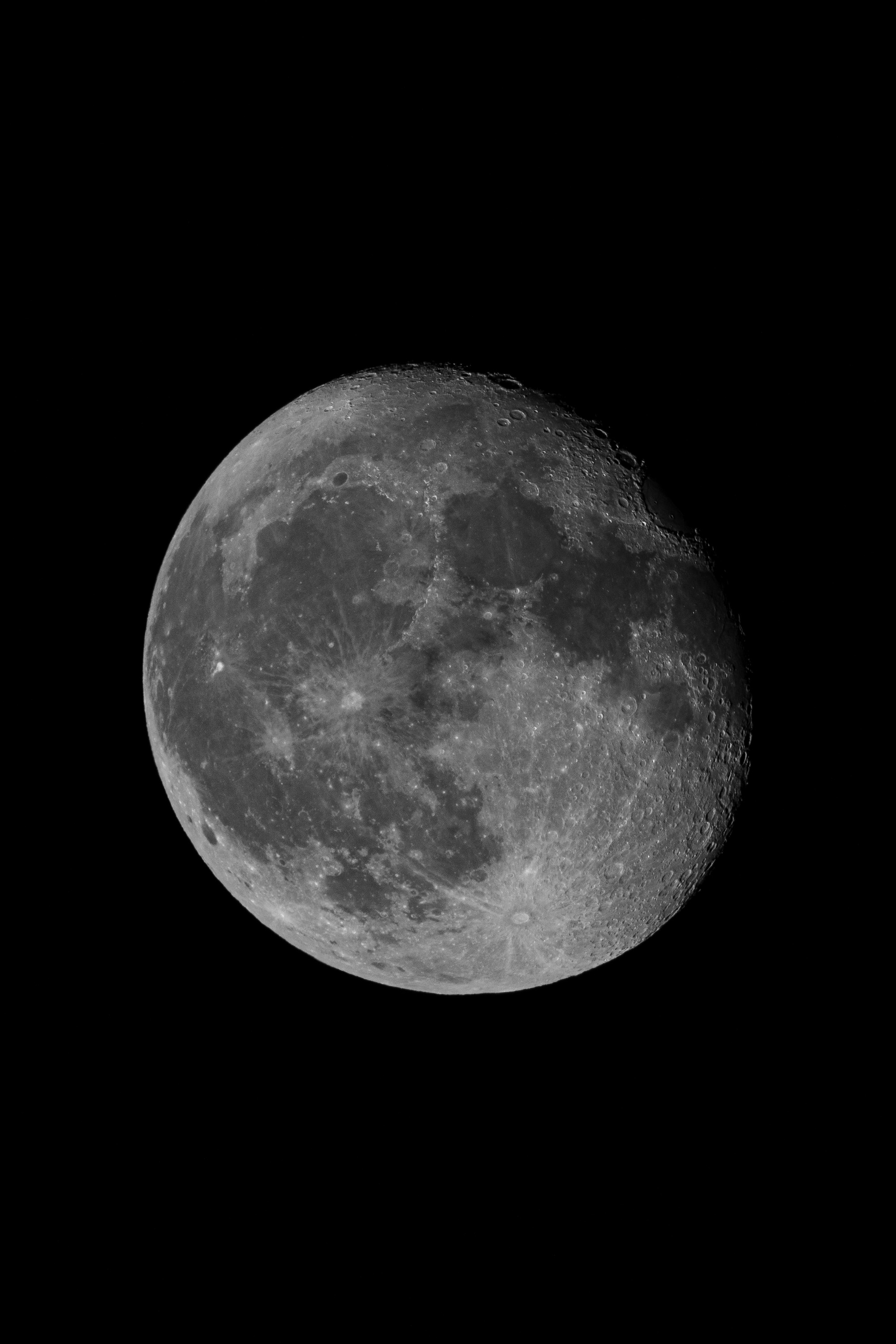 A nearly full moon illuminated against a black sky reveals detailed surface craters, maria, and highlands in stark grayscale contrast