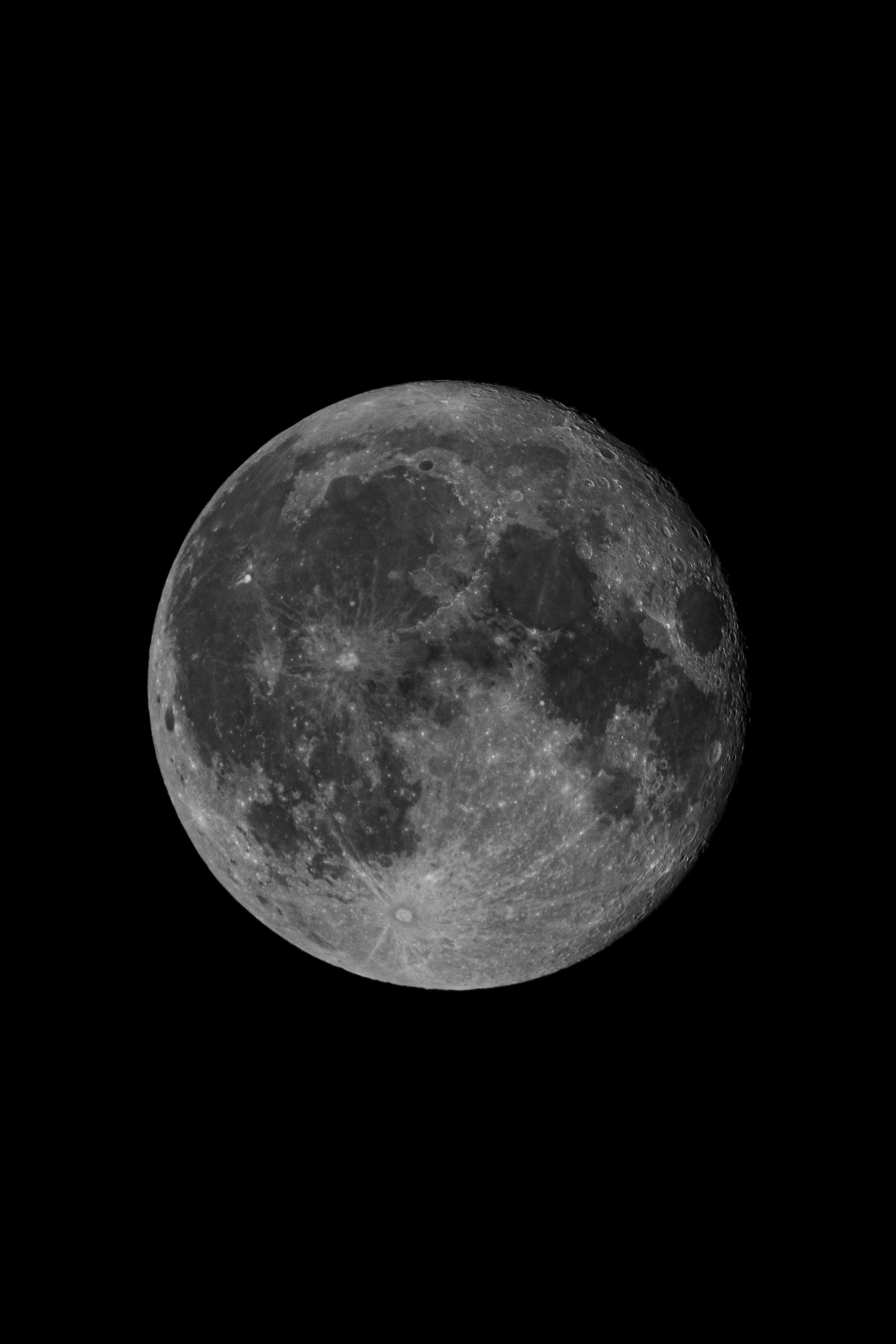 A full moon with detailed surface features including dark lunar maria and bright highlands stands against a pure black night sky