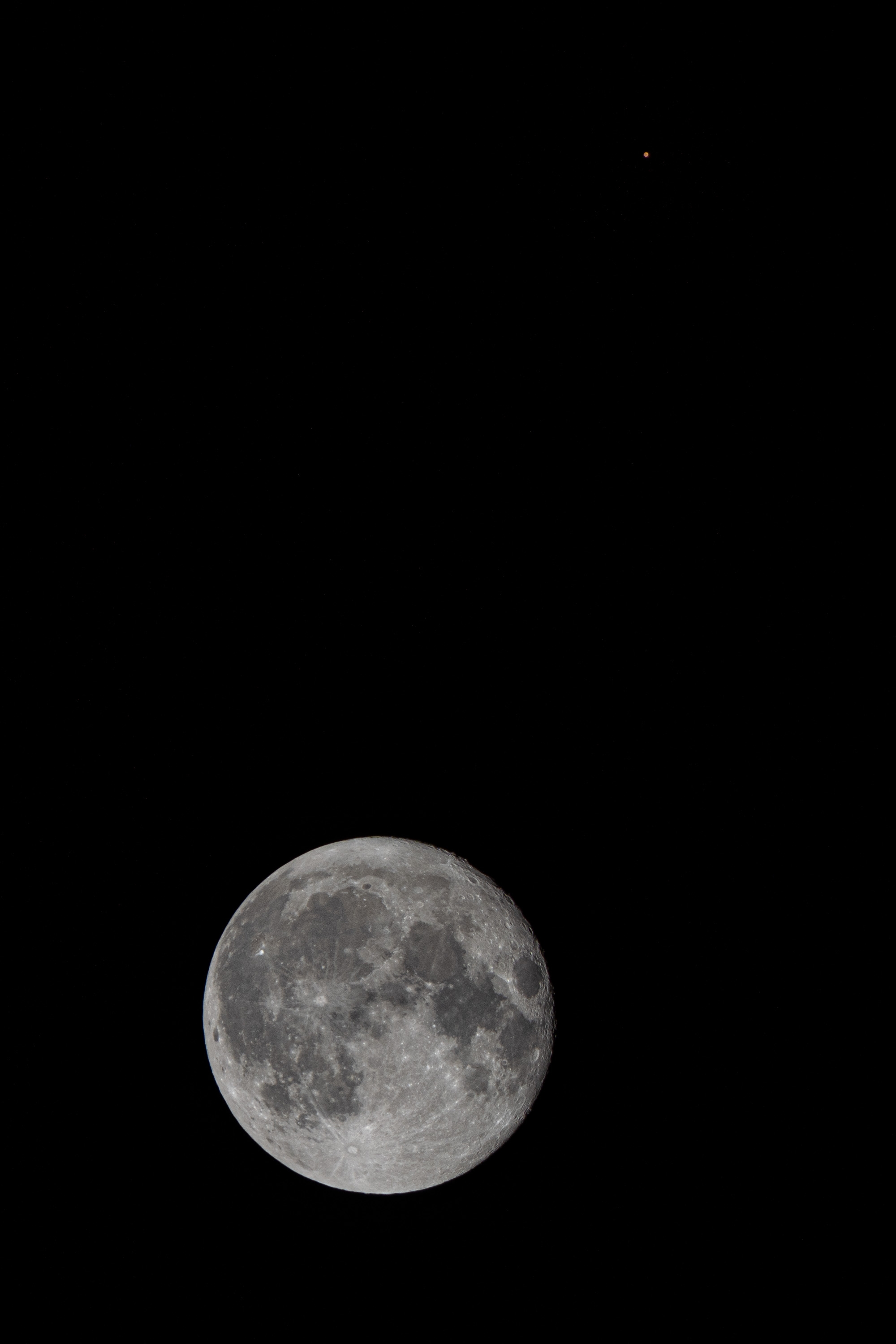 A fully illuminated moon positioned in the lower-left quadrant against a deep black night sky with a distant star visible in the upper right