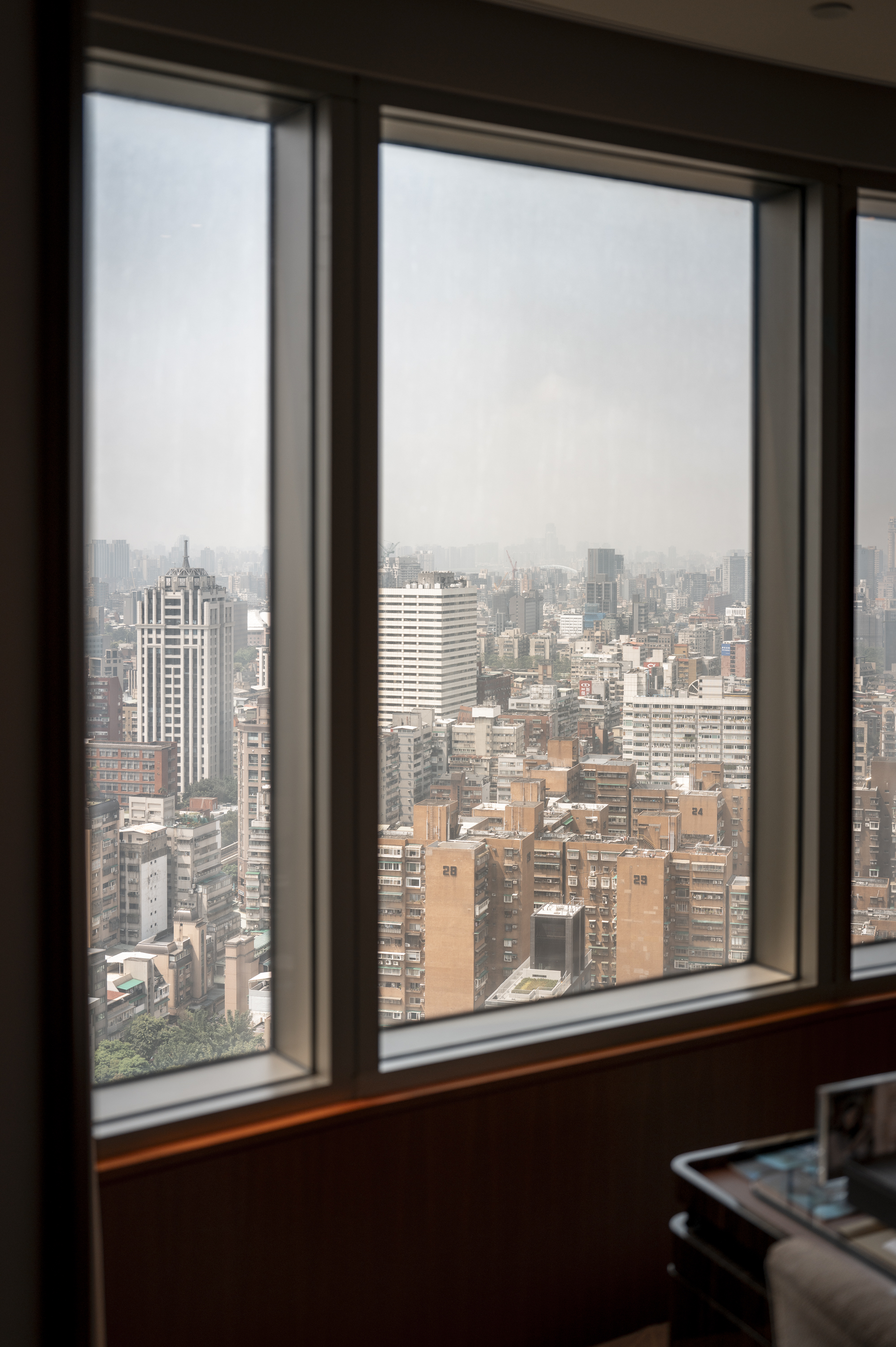 Panoramic view from a high-rise window reveals a dense urban skyline of Taipei with countless residential and office buildings under overcast daylight conditions
